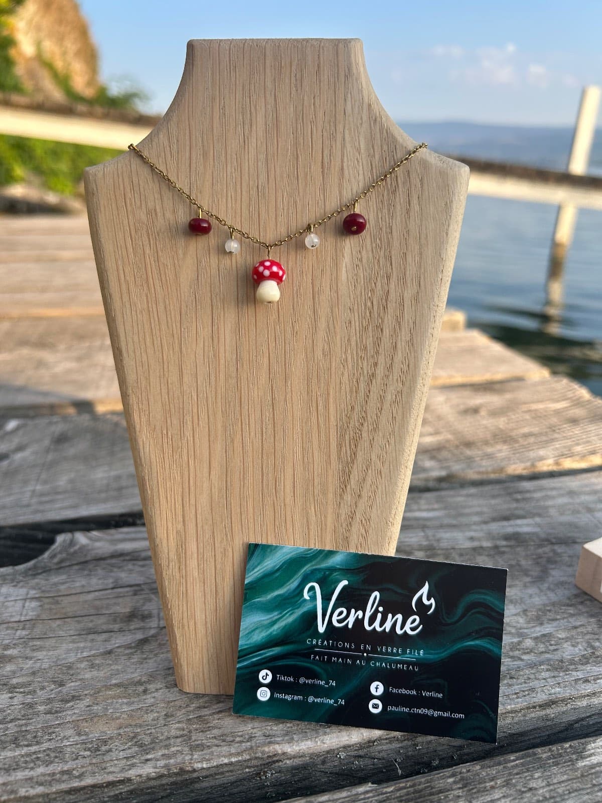 Collier chaîne dorée et pendentif champignon rouge à pois blancs présenté sur un buste en bois