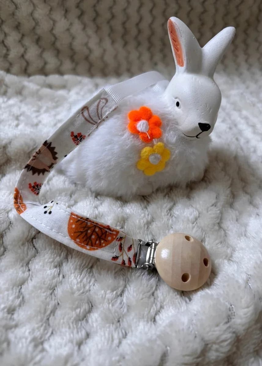 Attache-tétine en tissu imprimé d'automne avec clip rond en bois, posée près d'un lapin blanc décoratif.