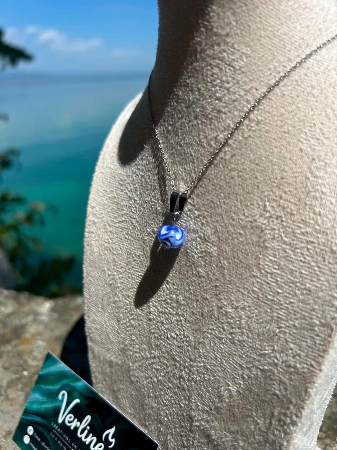 Gros plan sur le collier avec perle en verre filé bleue et blanche sur buste d'exposition.