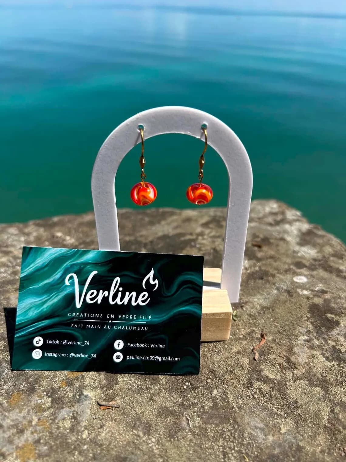 Vue de trois-quarts des boucles d'oreilles en verre filé orange et doré sur support en plein air.