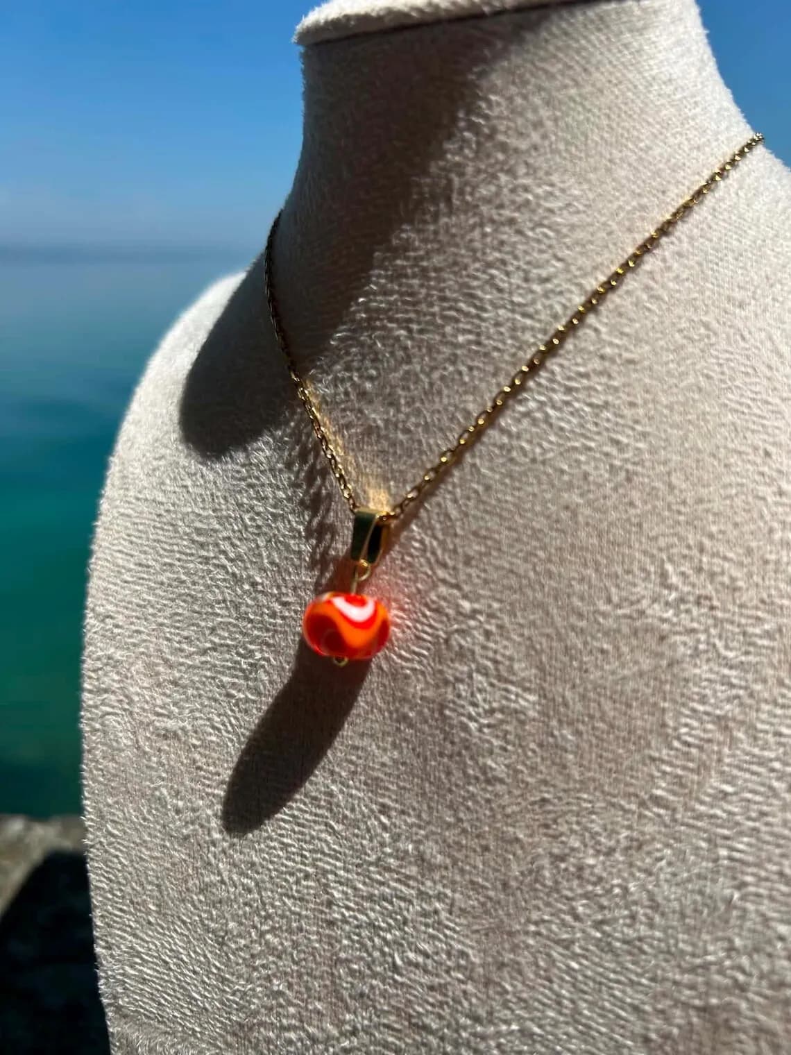 Gros plan sur le collier doré avec pendentif en perle de verre filé aux marbrures orange et blanches