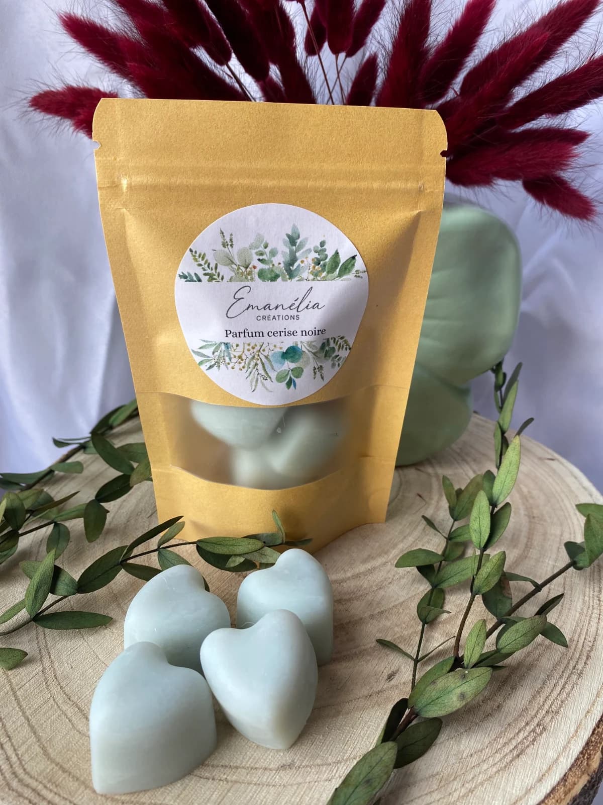 Sachet kraft et fondants parfumés en cœur présentés sur du bois avec des fleurs séchées bordeaux.